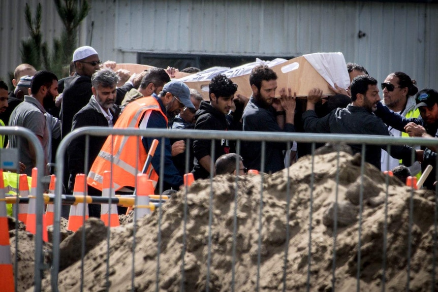 Men carry two bodies into a cemetery