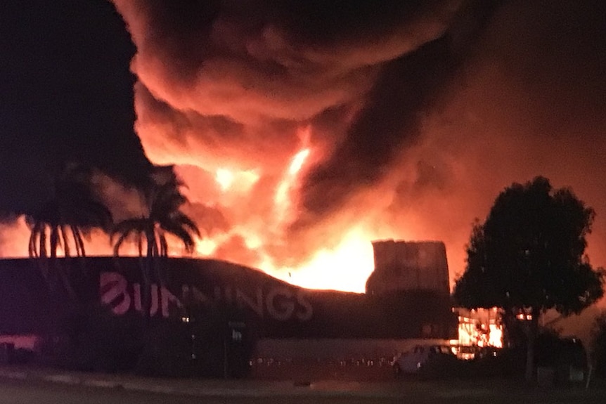 Thick plumes of smoke and bright orange flames fill a dark sky as a Bunnings store burns.