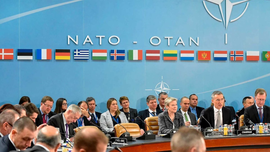 NATO members meeting with flags from nations behind them.