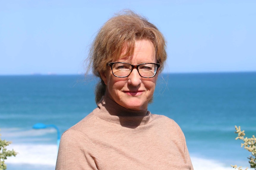 Profile shot of a woman with glasses and a beige top with the ocean in the background