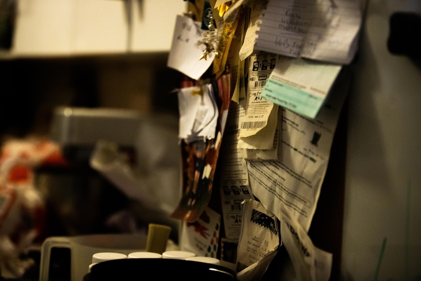 A clutter of receipts and notes pinned to a wall in a kitchen.