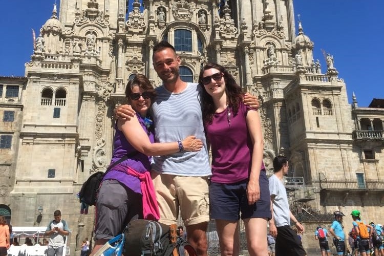 A man and two women hugging in front of a cathedral.