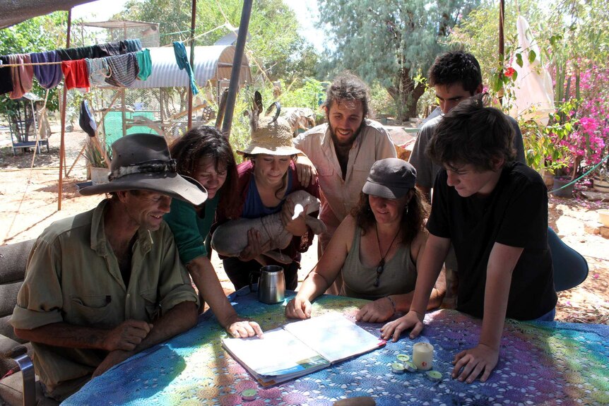 A group of people huddle tightly around a table pointing at a map.