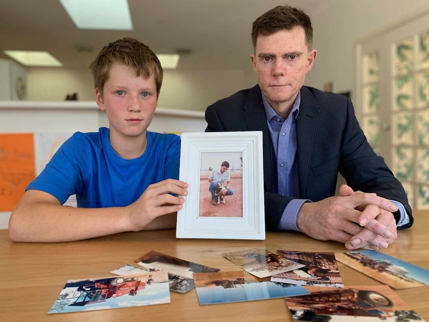 Robin, aged 11, sits next to his dad William and holds a framed picture of Greg with a dog on the farm.