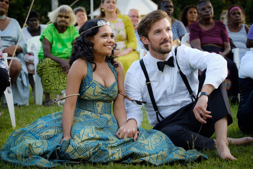 Well-dressed woman and a man sitting on the grass at an event.