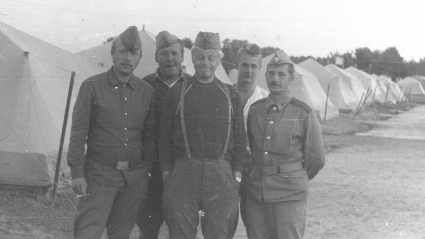 A black and white photo of five men in uniform standing in front of a row of white tents.