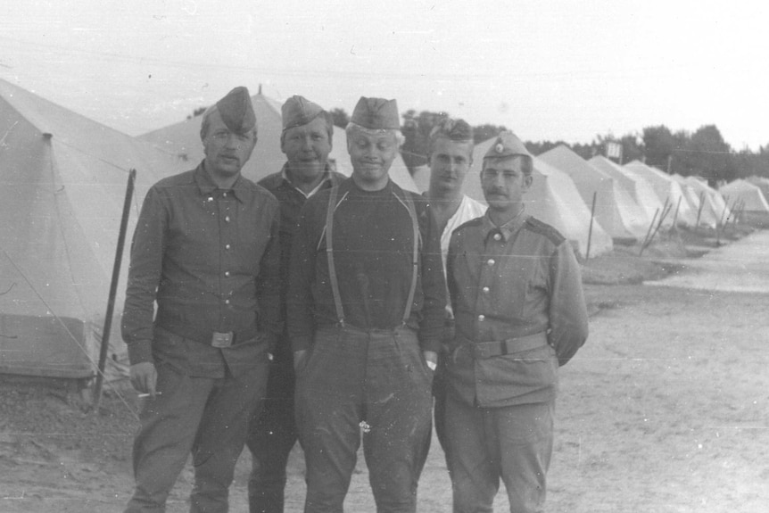 A black and white photo of five men in uniform standing in front of a row of white tents.