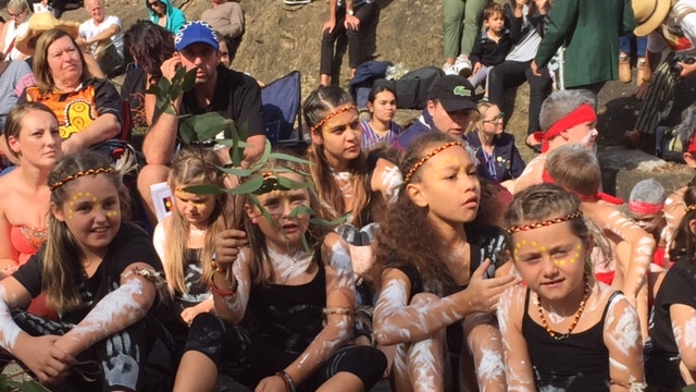 A group of children in traditional costume wear Indigenous paint on their skin.