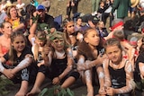 A group of children in traditional costume wear Indigenous paint on their skin.