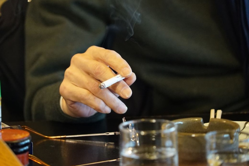A man holds a cigarette over an ashtray in a restaurant.