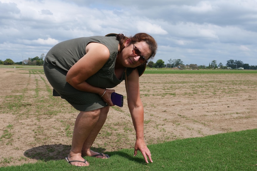 A woman inspects thick green grass on a farm