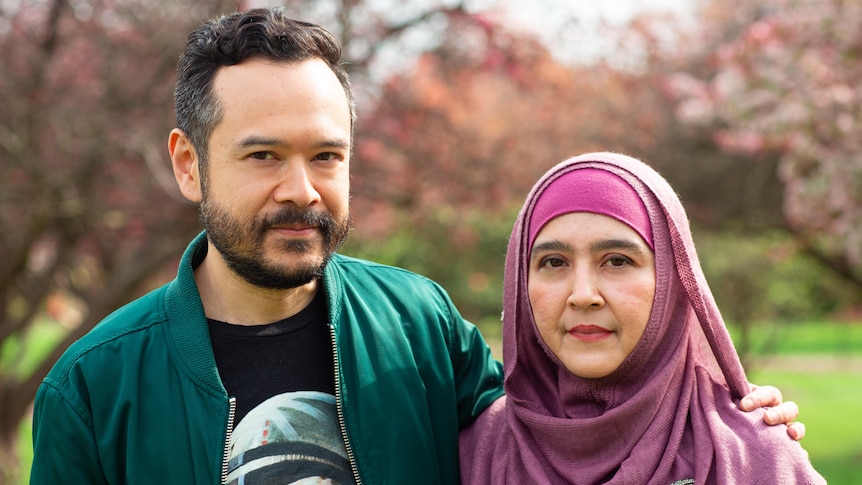 A man in a green jacket poses for a photo with his arm around a woman in a pink hijab