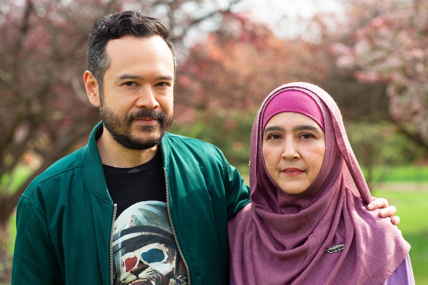 A man in a green jacket poses for a photo with his arm around a woman in a pink hijab