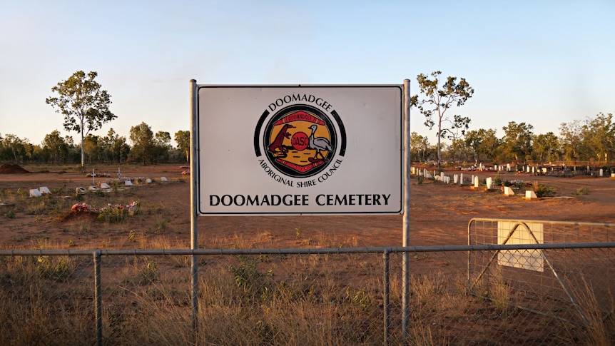 A red-dirt cemetery behind a sign that reads Doomadgee Cemetery