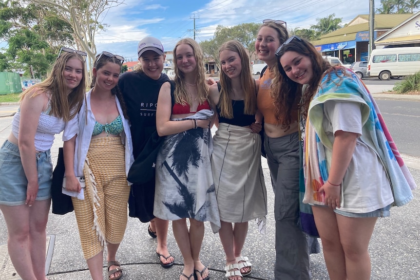 A group of young women in towels and swimwear pose on the street in Byron Bay.