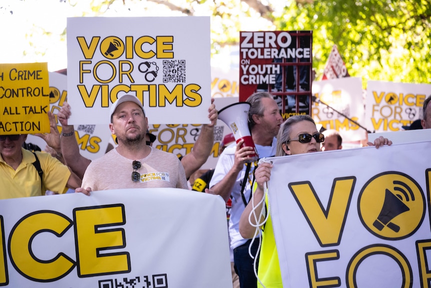 A group of protesters hold up signs saying 'voice for victims'. 