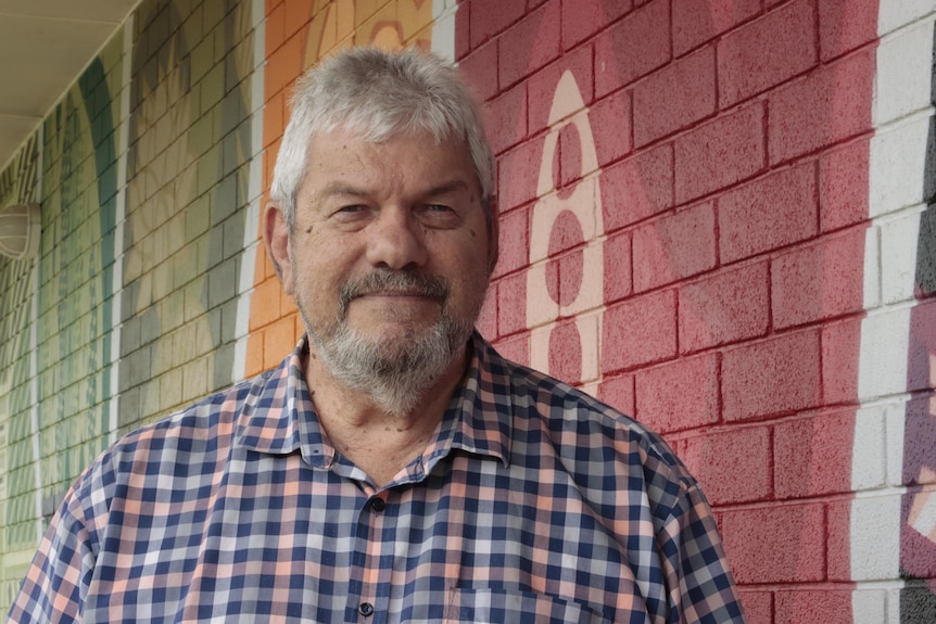 an aboriginal man with grey facial hair wearing a collared shirt