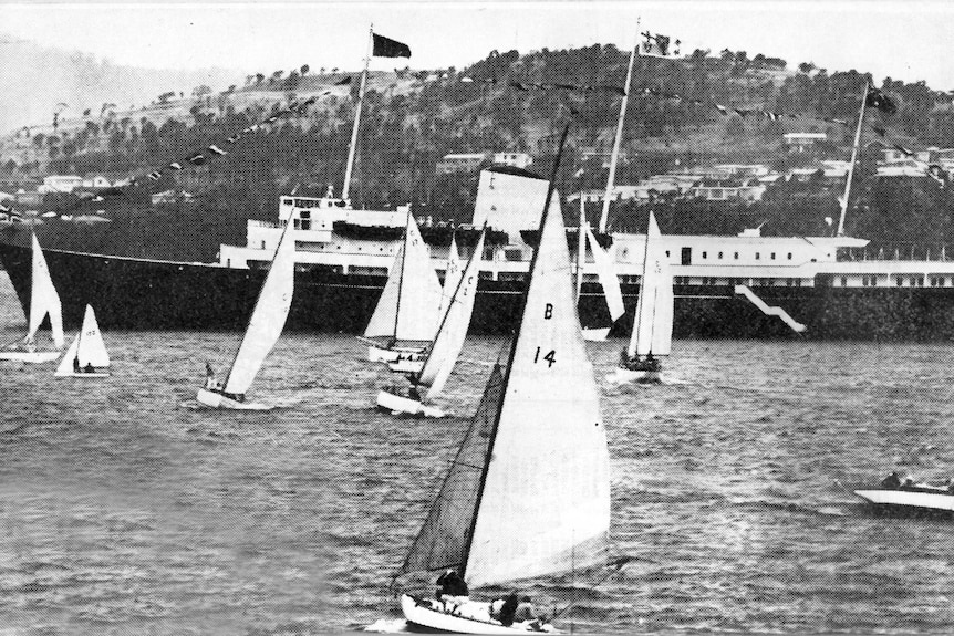 Black and white photo of a ship and several sailing boats