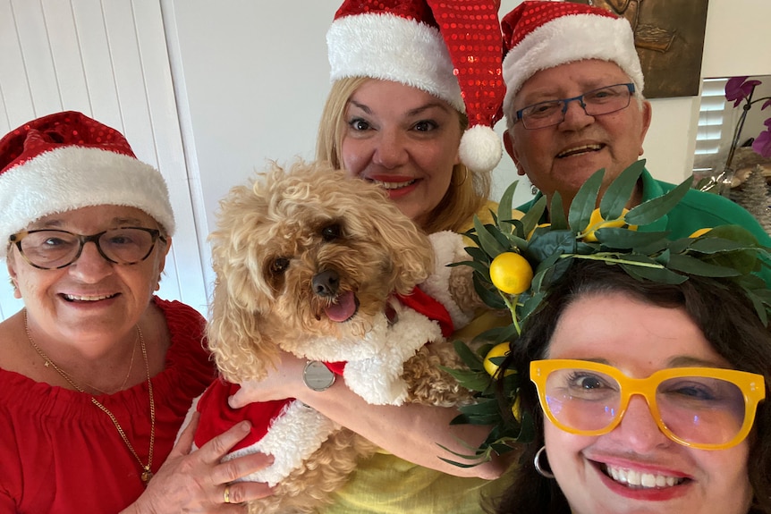 Smiling family dressed in festive hats pose with dog dressed in a Santa coat. 