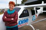One Nation part leader Pauline Hanson stands in front of a light plane.