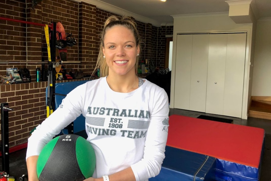 Laura in a garage holding a 5kg medicine ball with gym equipment in the background.