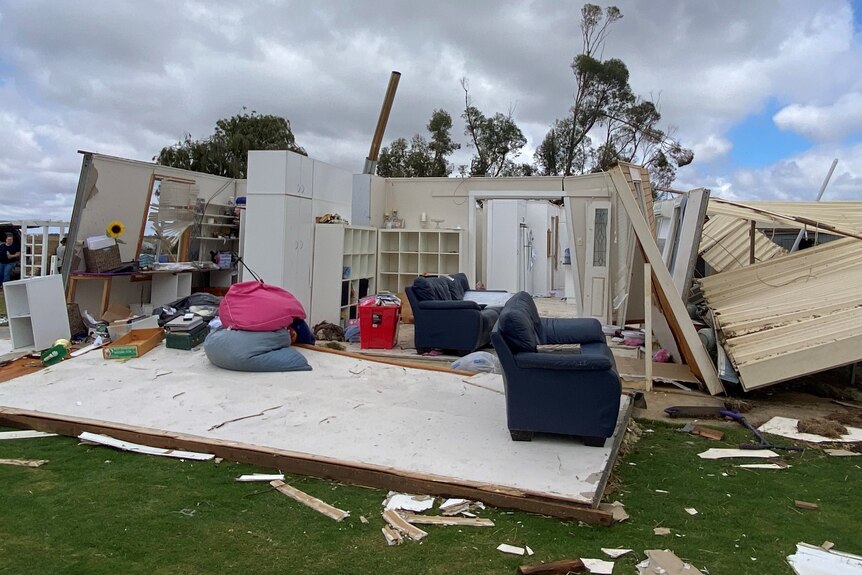 Home with walls and roof ripped off, showing into lounge and bedroom, trees in background