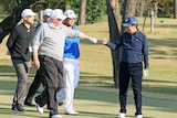US President Donald Trump fist pumps Japan's Prime Minister Shinzo Abe on a golf course as others watch on.