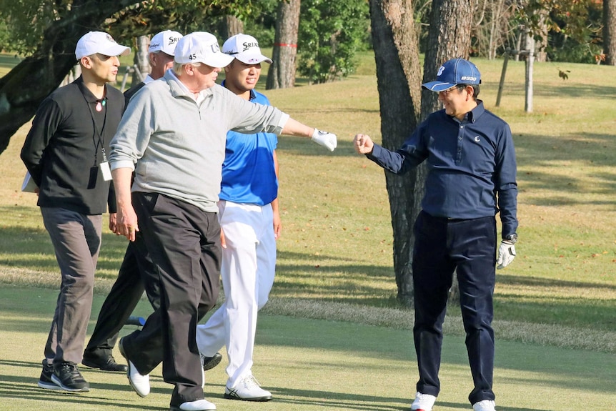 US President Donald Trump fist pumps Japan's Prime Minister Shinzo Abe on a golf course as others watch on.