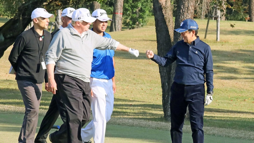 US President Donald Trump fist pumps Japan's Prime Minister Shinzo Abe on a golf course as others watch on.