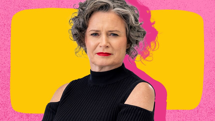 Comedian Judith Lucy looking serious and wearing a black long-sleeved top with shoulder cutouts and red lipstick. 