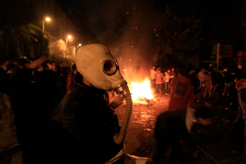 An Egyptian protester wearing a gas mask walks past a fire lit during clashes in Cairo.