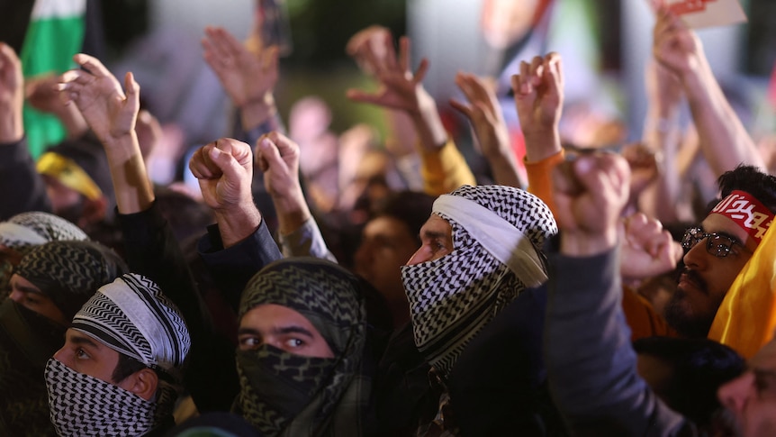 A crowd of people raise their hands in the air at a gathering in Iran.