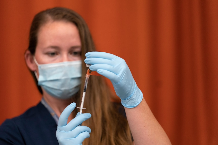 A woman in a mask and disposable gloves draws a vaccine with a syringe. 