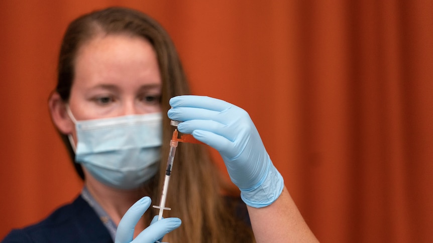 A woman in a mask and disposable gloves draws a vaccine with a syringe. 