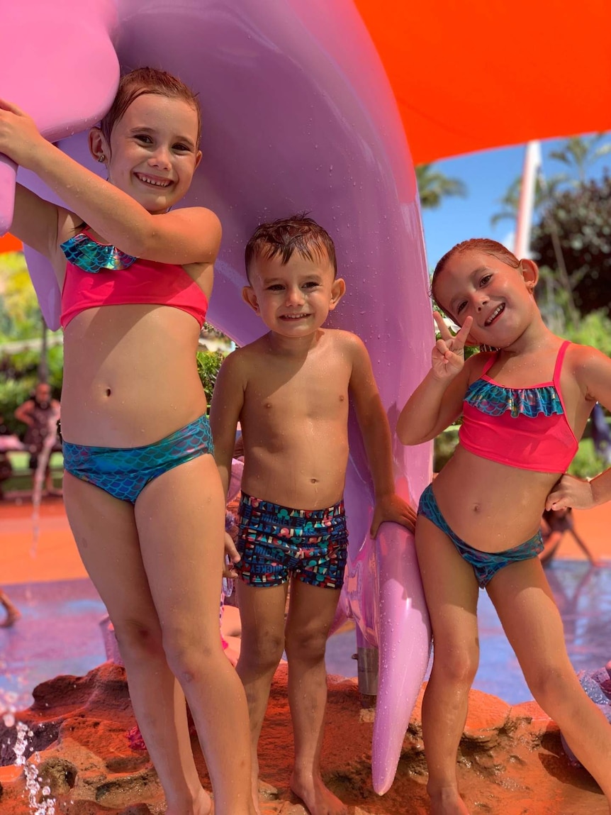 Three kids smile and pose at a colourful waterpark.