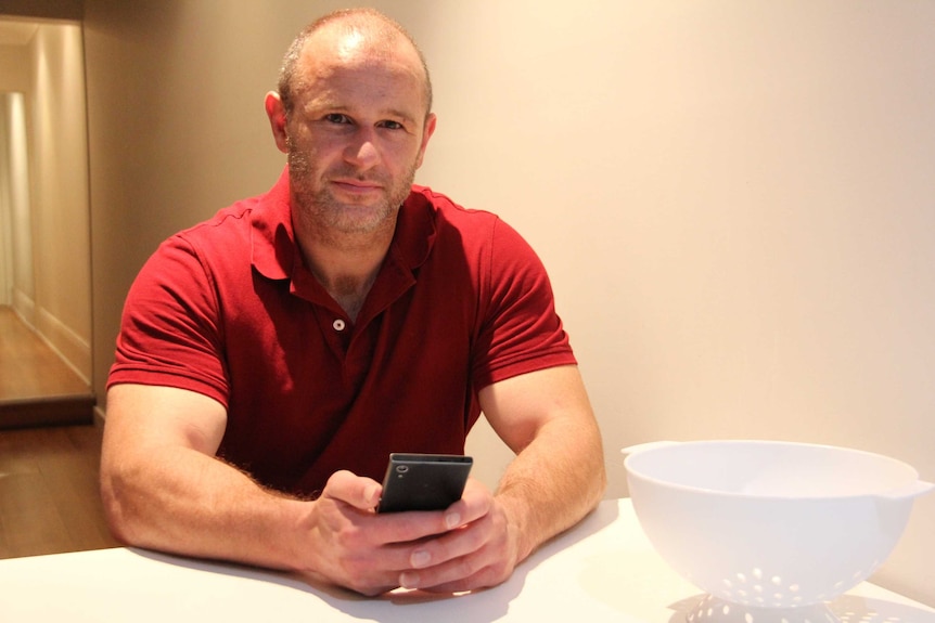 A man in a red shirt holds a smartphone.