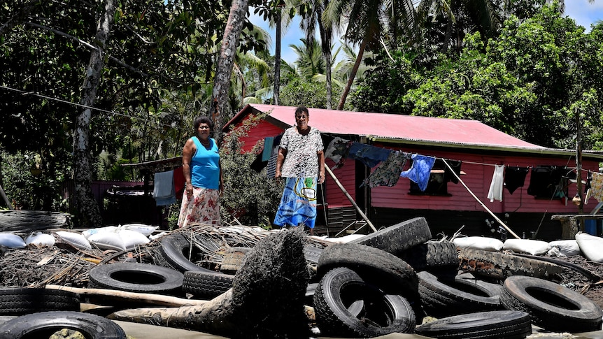 Lavenia McGoon with a family member standing past a makeshift seawall of old rubber car tyres to prevent erosion