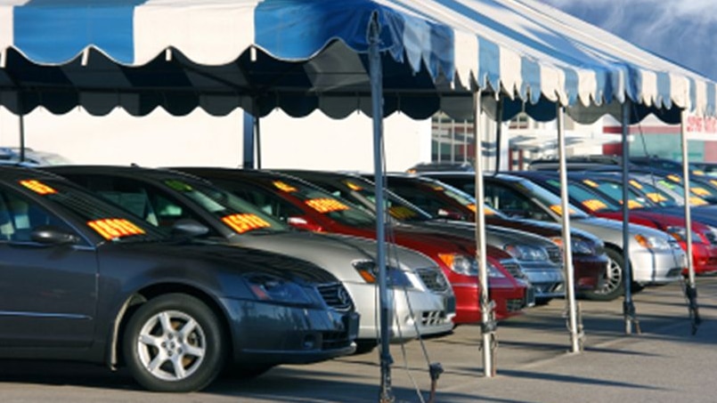 used car yard with different coloured cars under a blue and white striped awning