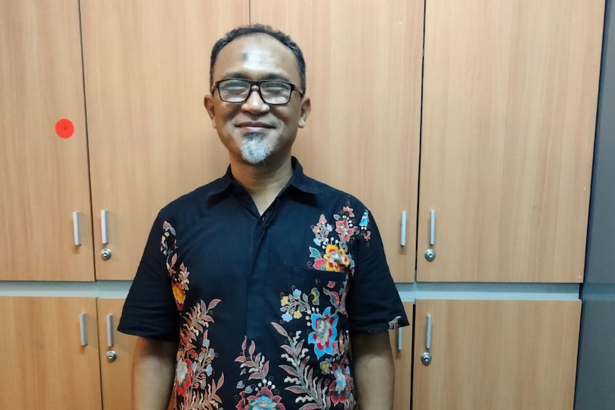 Mohamed Lotfi berdiri di depan lemari dan tersenyum untuk foto dari pinggang ke atas.