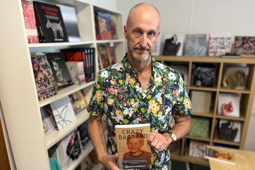 man holding book in front of shelves of books