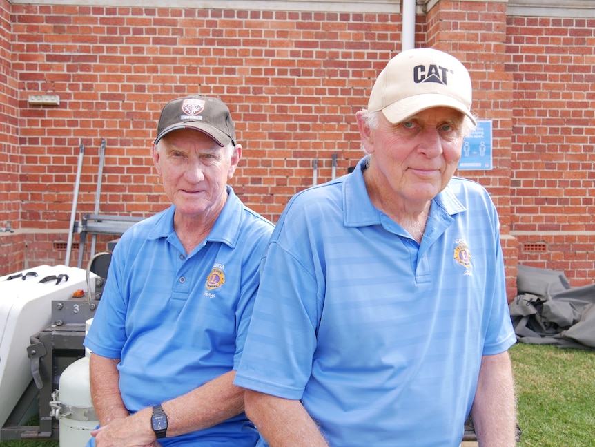 Two men in their 70s sitting outside a brick building.