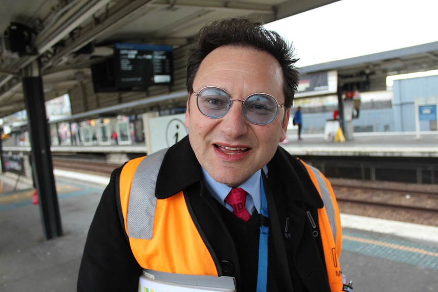 A man in a high-vis vest on a train platform, smiling and very happy.