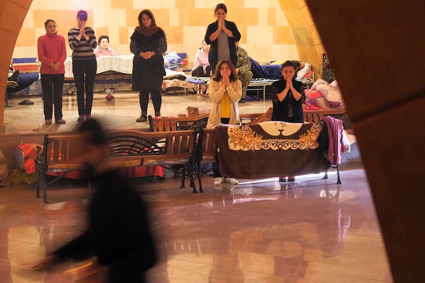 Several women pray amongst makeshift beds in an improvised bomb shelter.