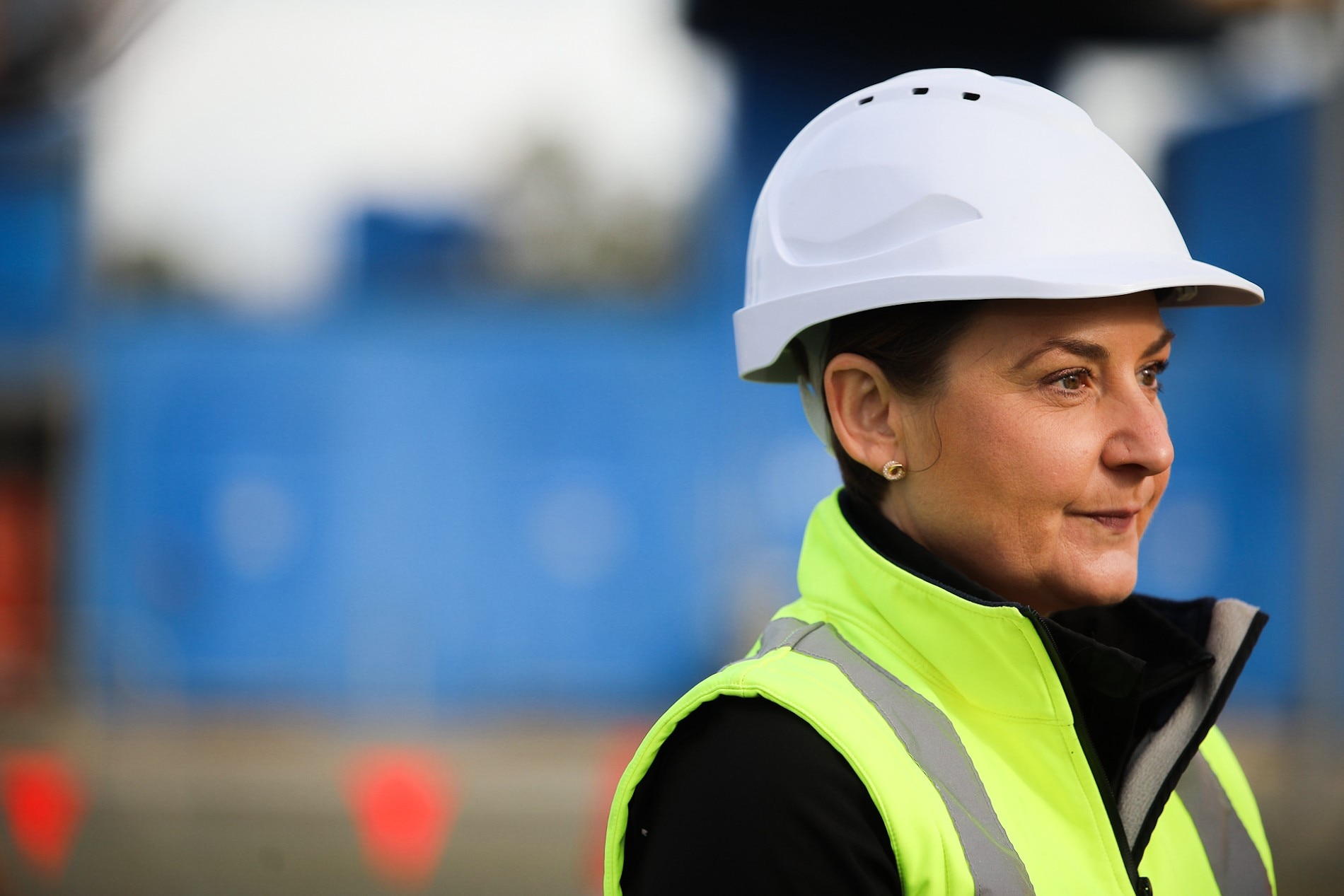 A woman in a hard had and a high-viz vest stares into the distance 