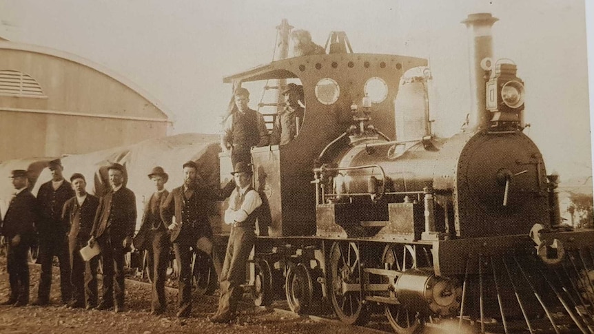 A large group of railway men stand next to a train with Bob the dog sitting on top.