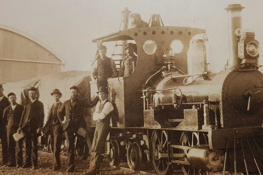 A large group of railway men stand next to a train with Bob the dog sitting on top.