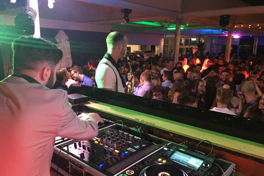 A DJ handles a mixing board as a crowd of people party on.