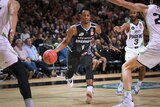 An NBL basketballer dribbles with the ball as defenders close in on him.