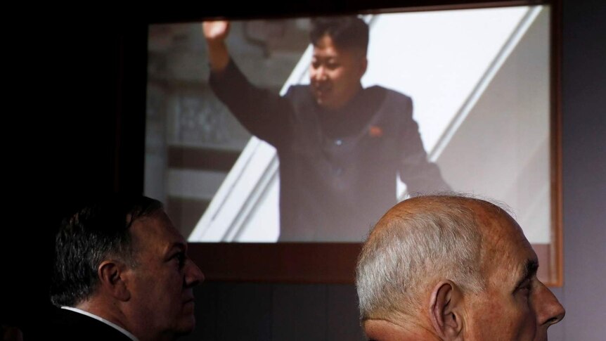 Movie sill of Kim Jong-un on a big screen in background with Mike Pompeo and John Kelly in foreground