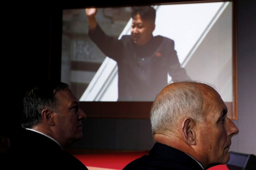 Movie sill of Kim Jong-un on a big screen in background with Mike Pompeo and John Kelly in foreground
